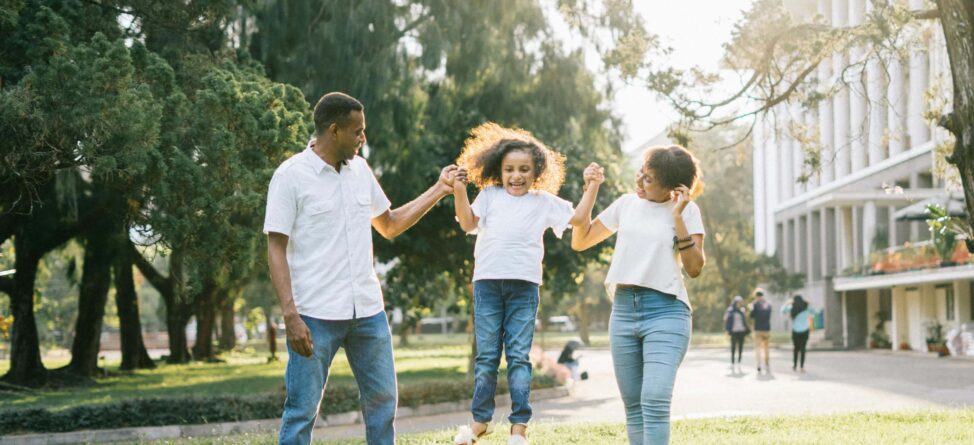 Happy family walking outdoors, lifting their child between them on a sunny day