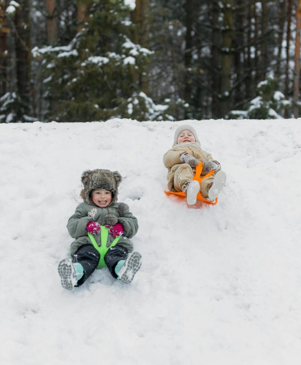 Two young children sledding down a snowy hill with big smiles on their faces