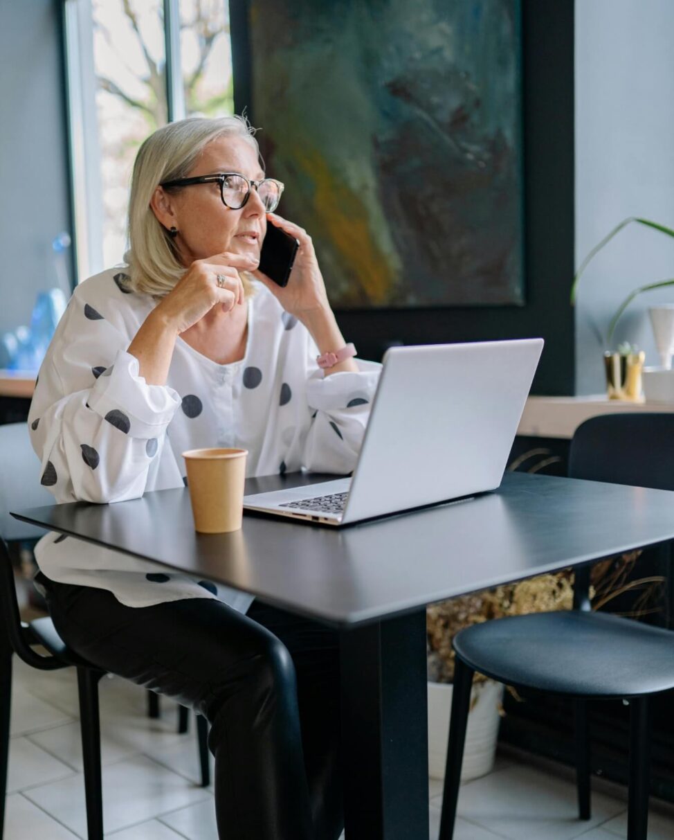 Woman on a phone call while working on a laptop in a modern cafe