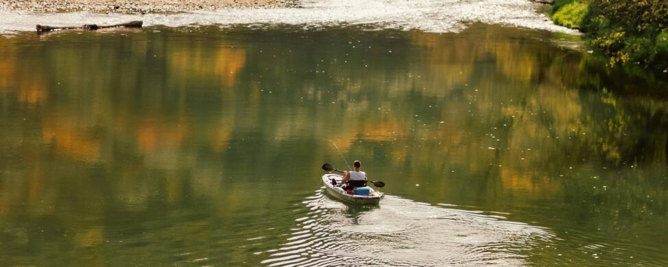 Man kayaking on a calm river with reflections of fall trees